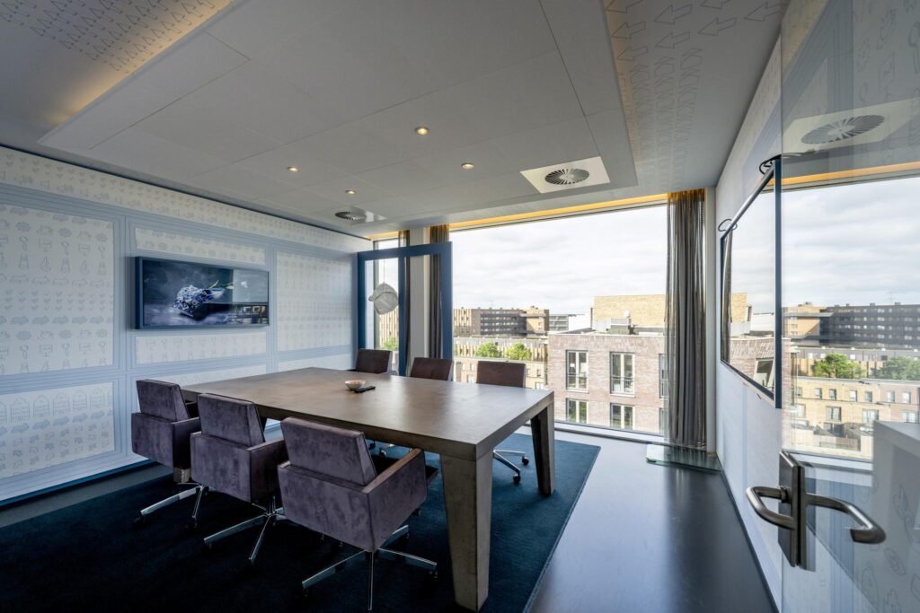 Modern meeting room with a large wooden table, purple chairs, and a view over Krijn Taconiskade in Amsterdam.